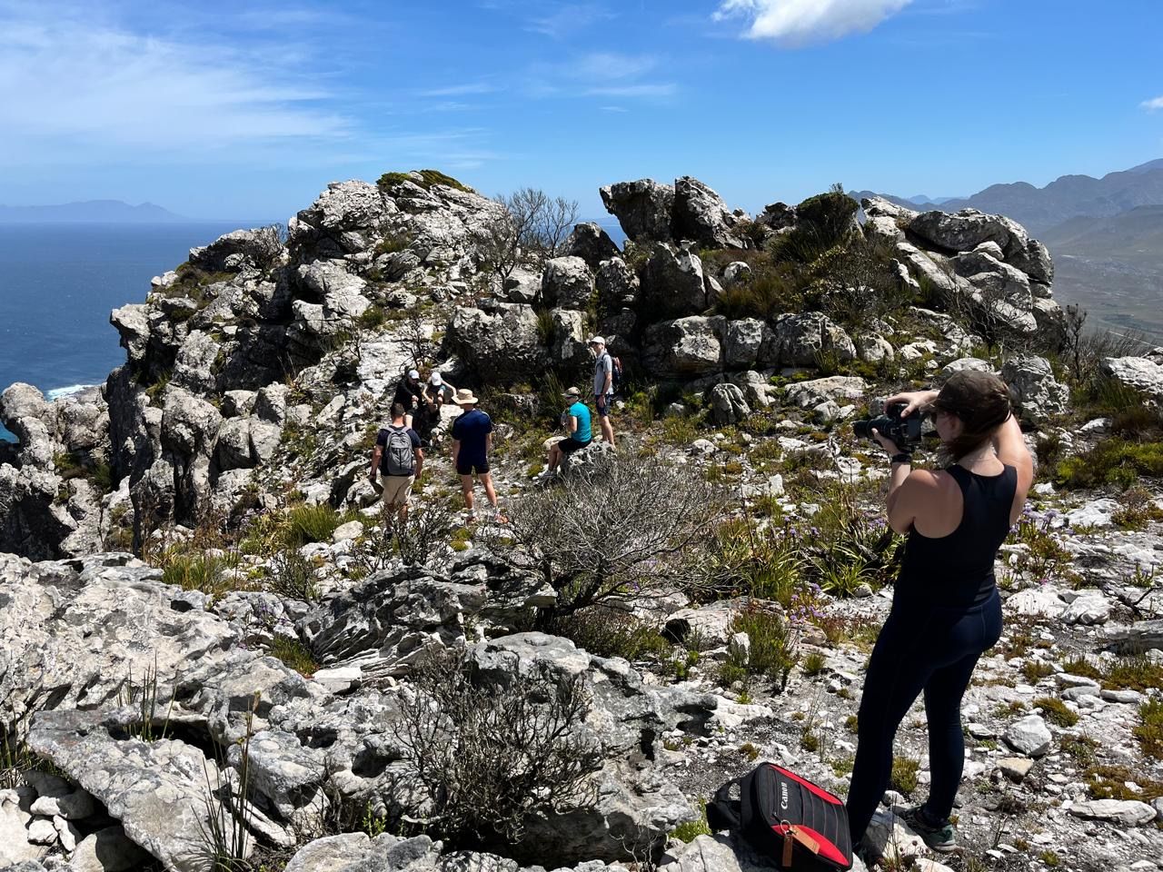 Hikers climbing rocky mountain terrain with ocean views and blue sky in Cape Town, South Africa.