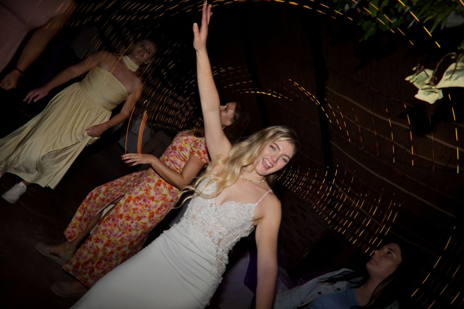 A bride in a white dress raises her arm joyfully on the dance floor at a wedding reception.
