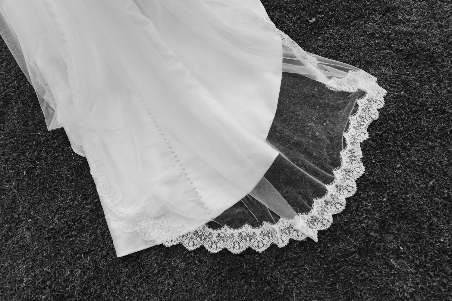 Black and white photo of a bridal veil with delicate lace trim spread on dark ground.