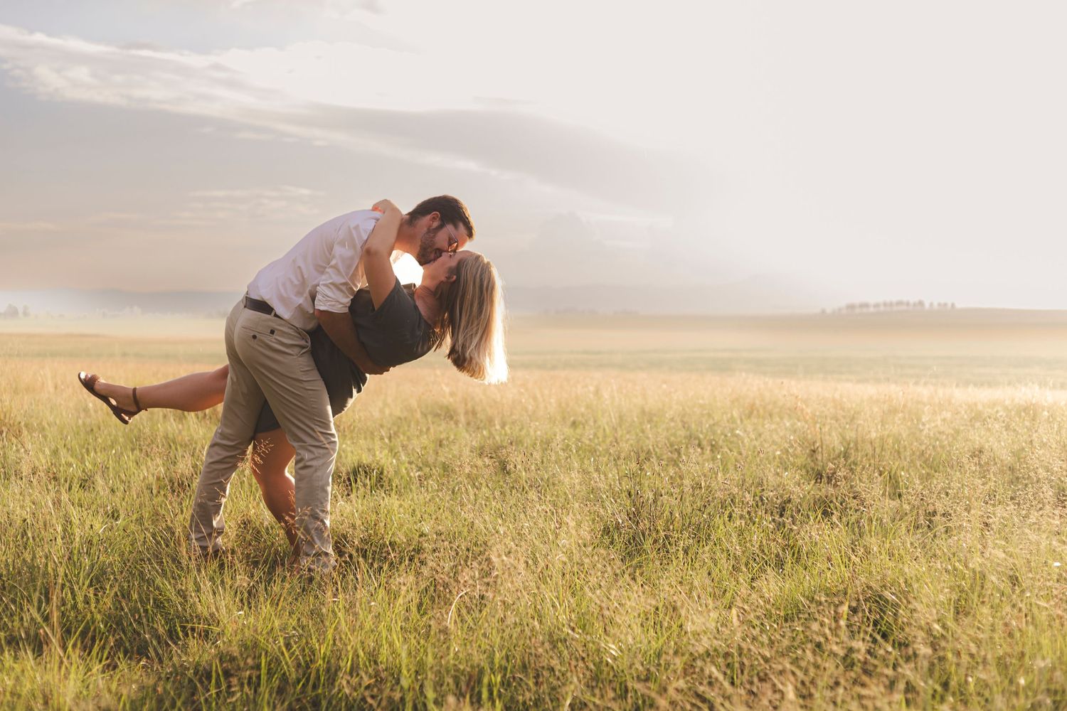 Romantic couple dancing and dipping in a golden wheat field at sunset.