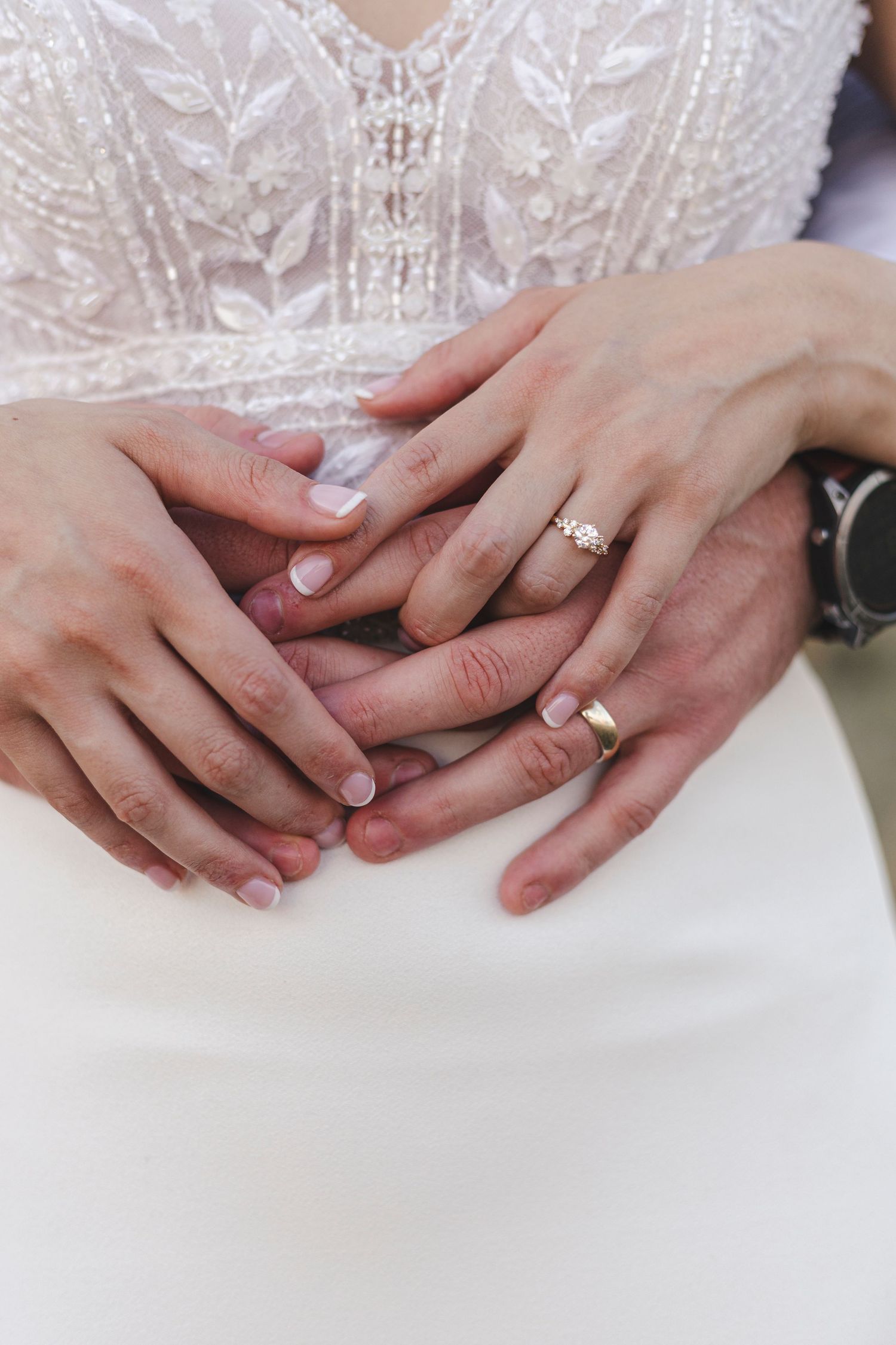 Close-up of hands showing wedding rings against a white lace dress bodice.