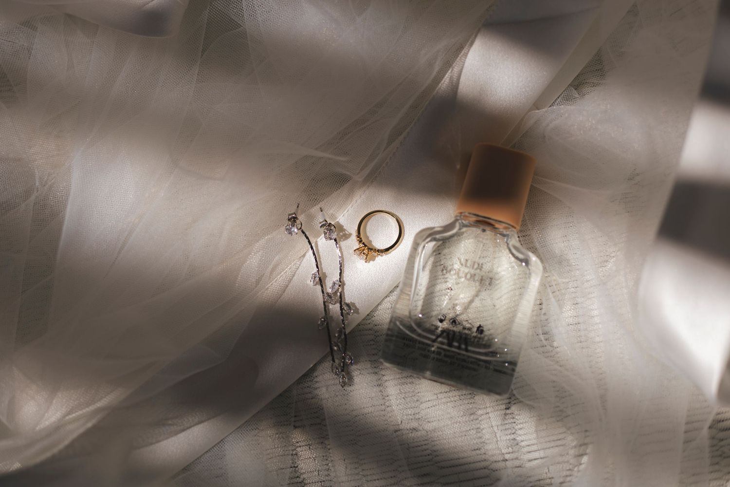 Wedding rings and perfume bottle artistically photographed with soft shadows.