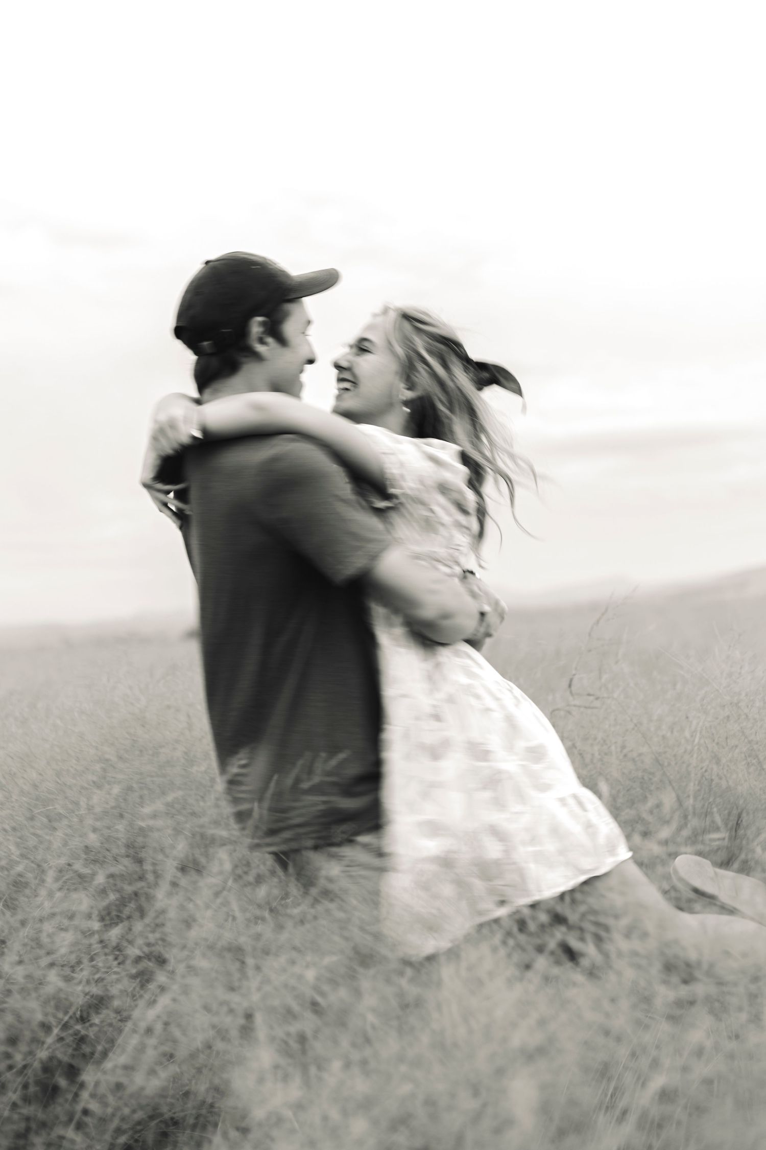 Black and white photo of couple spinning and laughing in a grassy field.