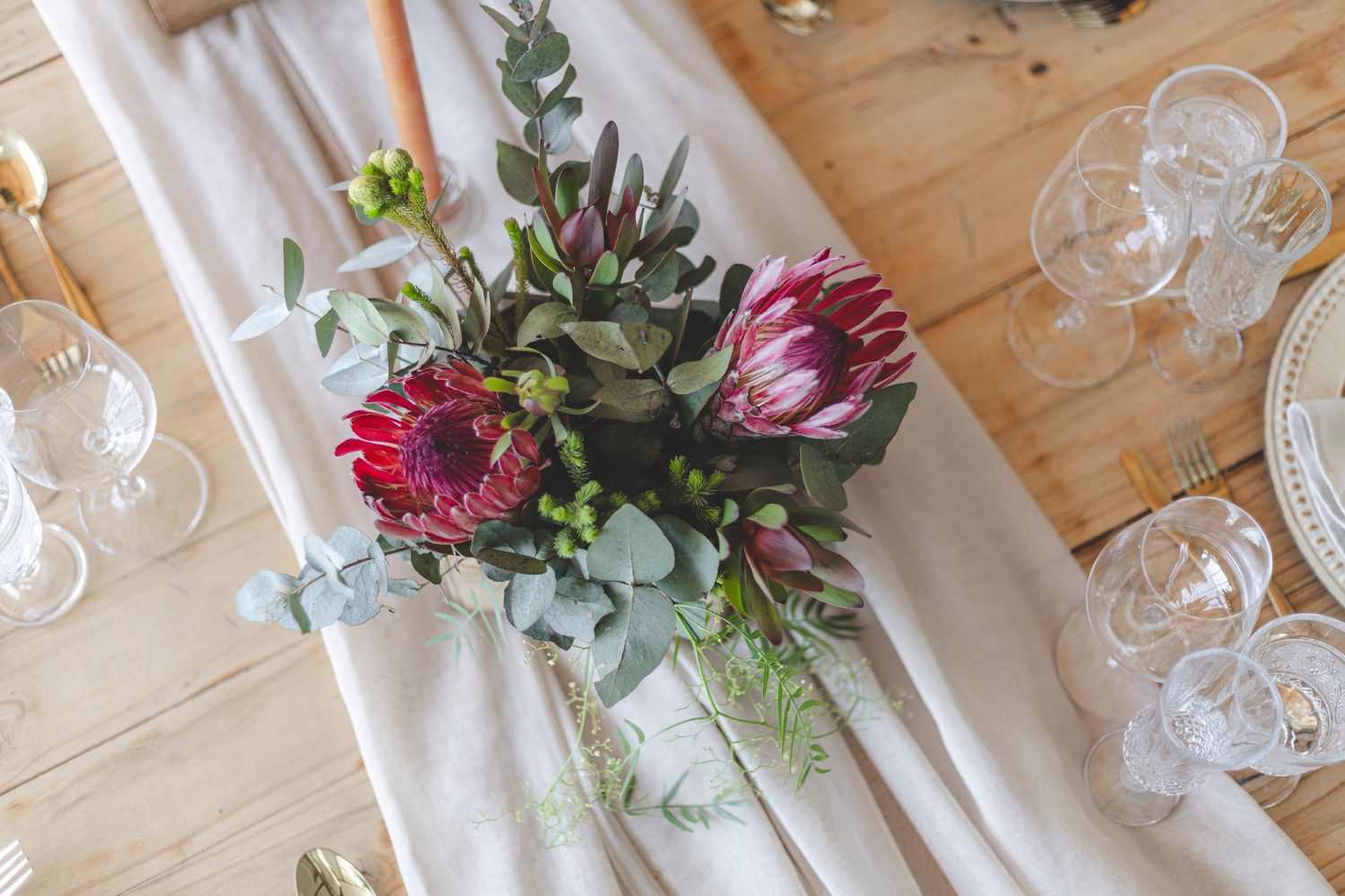 Close up of protea and eucalyptus flower arrangement on white table runner.