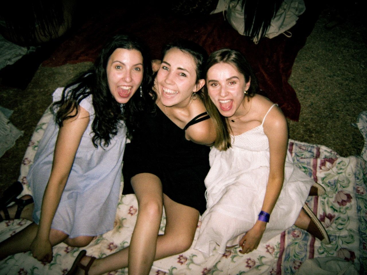 Three young women smiling and sticking out tongues, posing together at a casual indoor gathering.