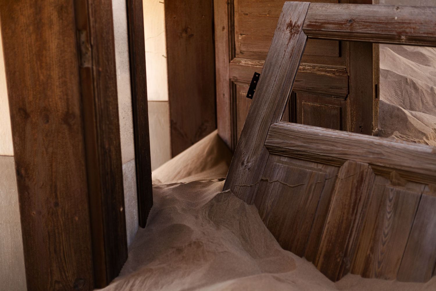 Sand drifts through wooden doorways in an abandoned desert structure.