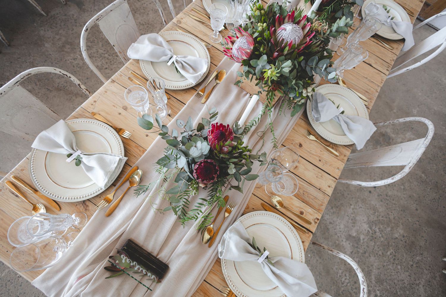 Overhead view of wedding table settings with burgundy floral centerpieces and white chairs.