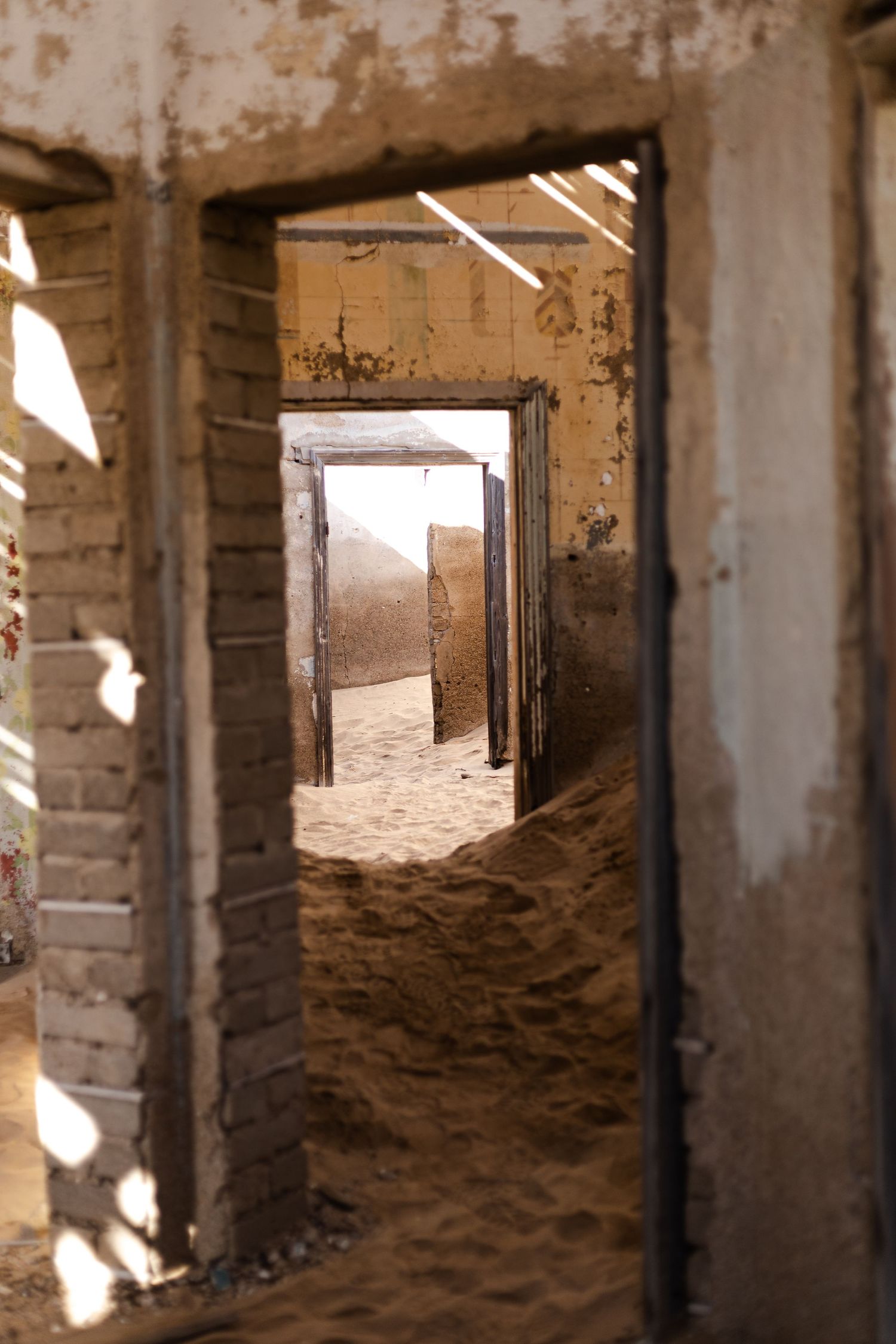 Sandy corridor through abandoned building with sunlight casting dramatic shadows.