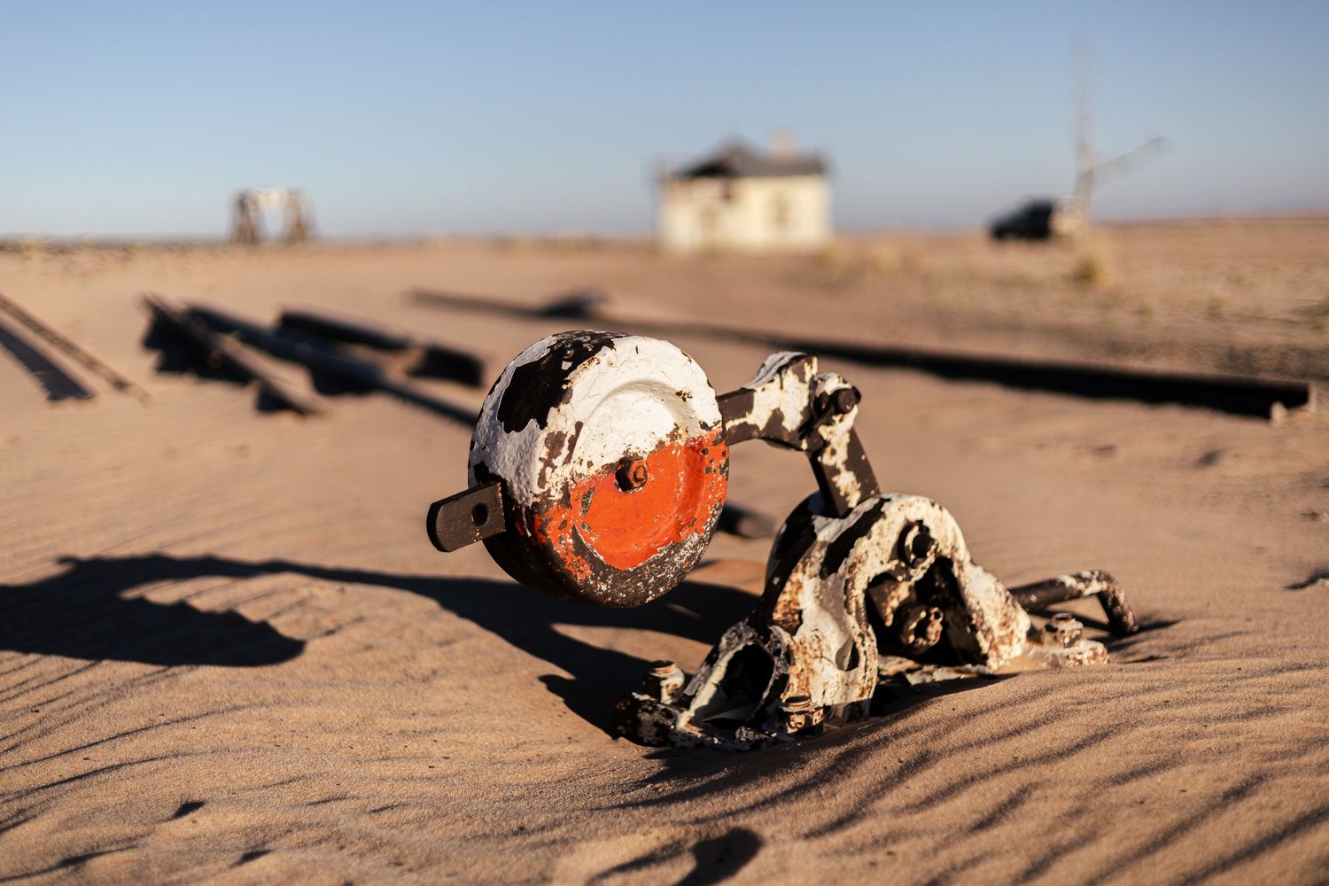 Old rusted railroad signal light lies abandoned in desert sand casting long shadows.