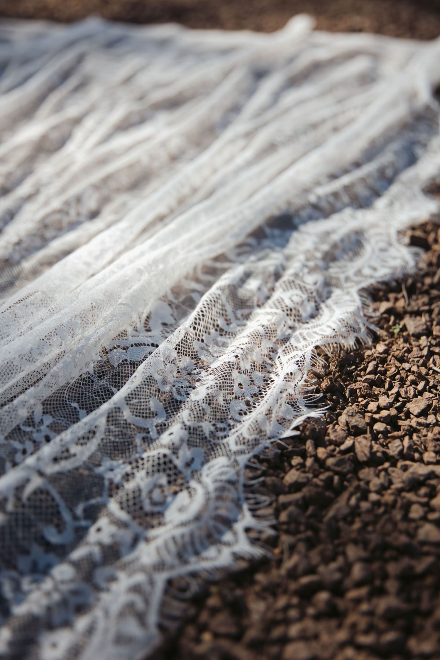 White lace wedding veil draped over rustic rocky ground, showcasing delicate floral lace trim detail in natural outdoor setting.