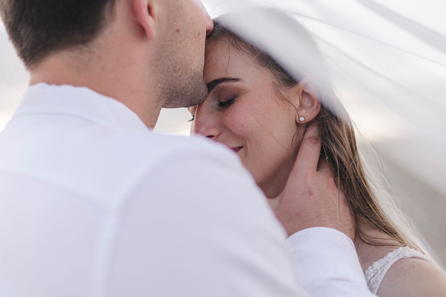 Intimate moment between newlyweds under white veil.