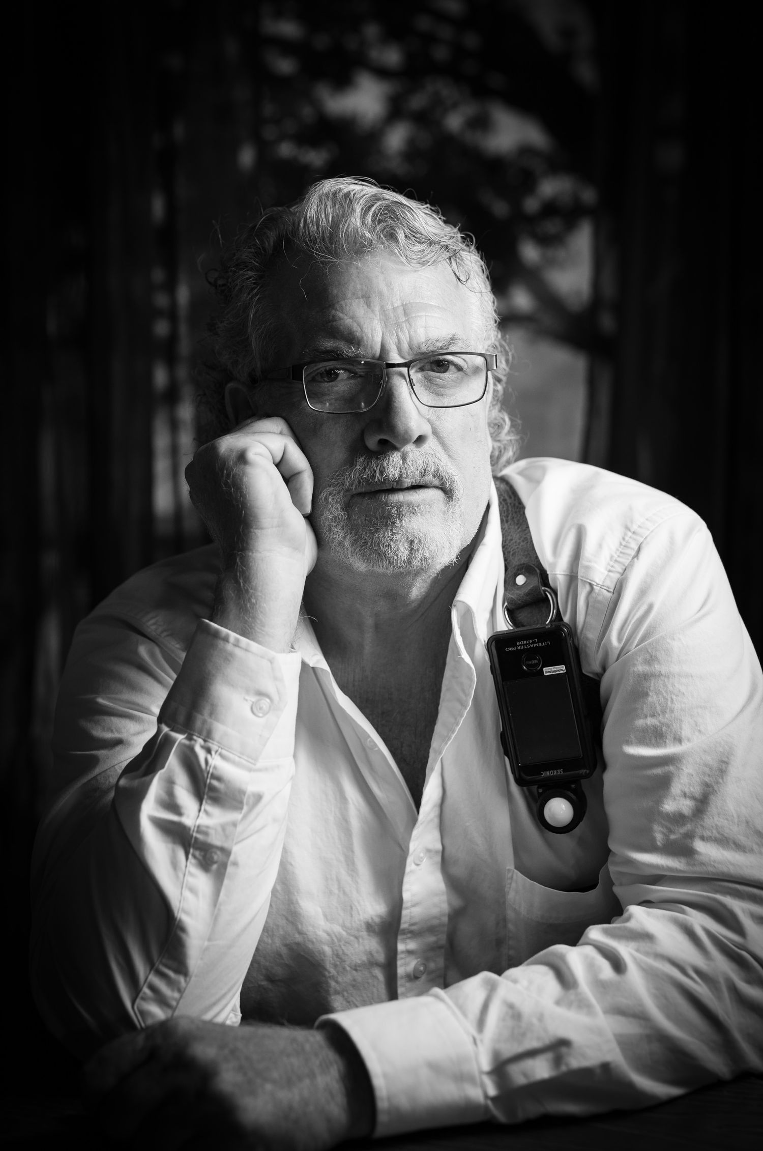 Black and white portrait of a person in glasses and white shirt holding a walkie talkie while resting hand on chin.