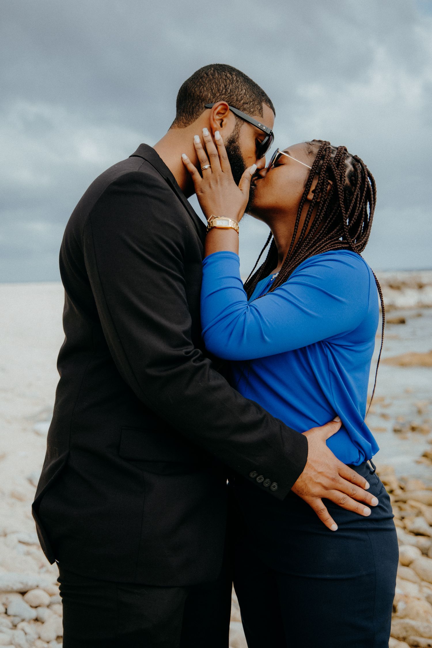 Couple in black and blue sharing intimate moments during a beachside photoshoot.