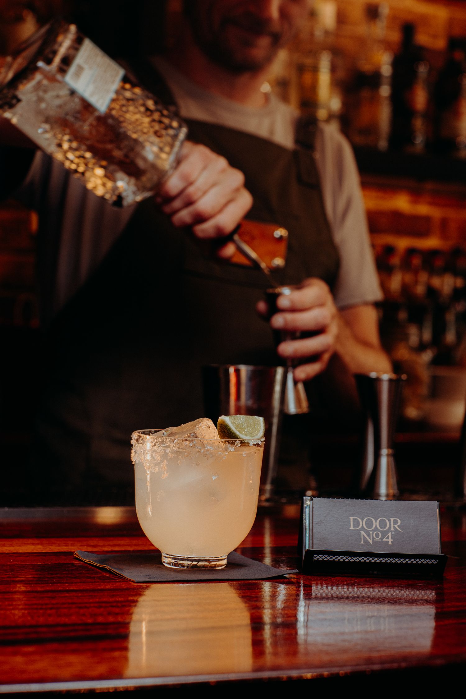 A bartender pours a cocktail at a dimly lit bar with a Door No 2 sign visible.