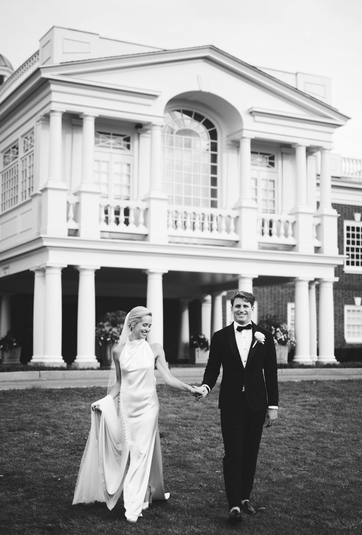 Classic black and white wedding photo at Philadelphia Cricket Club with the couple walking in front of the grand clubhouse architecture.