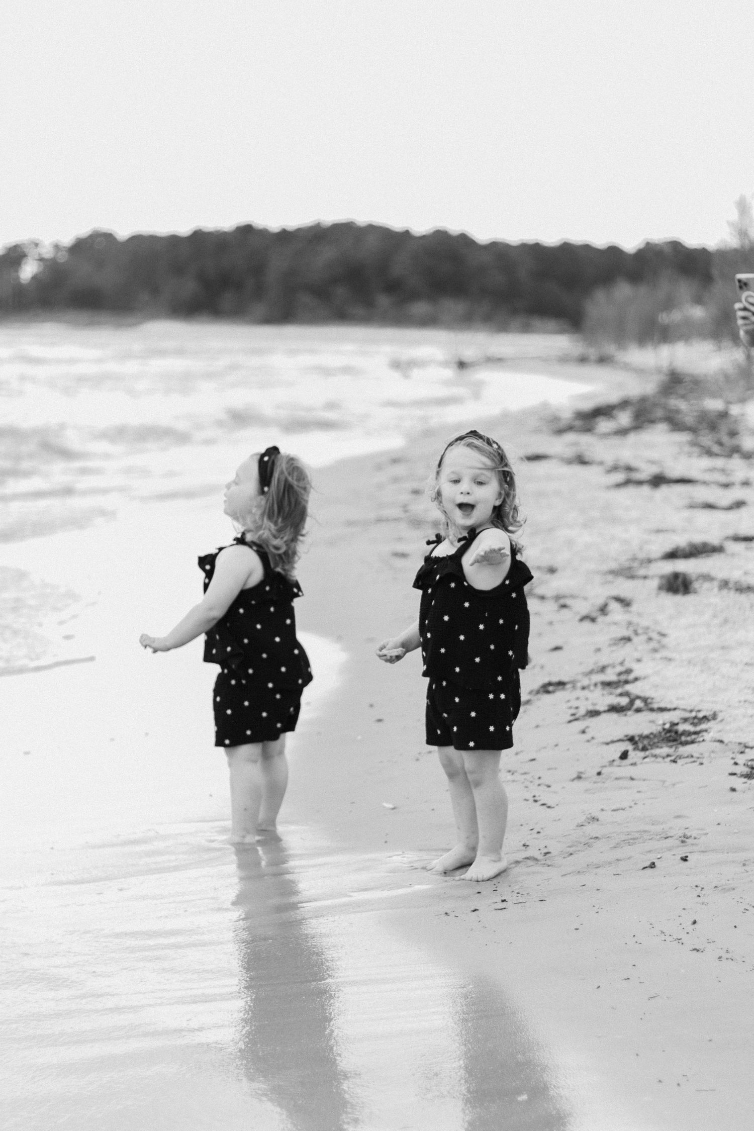 A series of black and white photos shows joyful play at the beach in polka dot swimsuits near ocean waves.