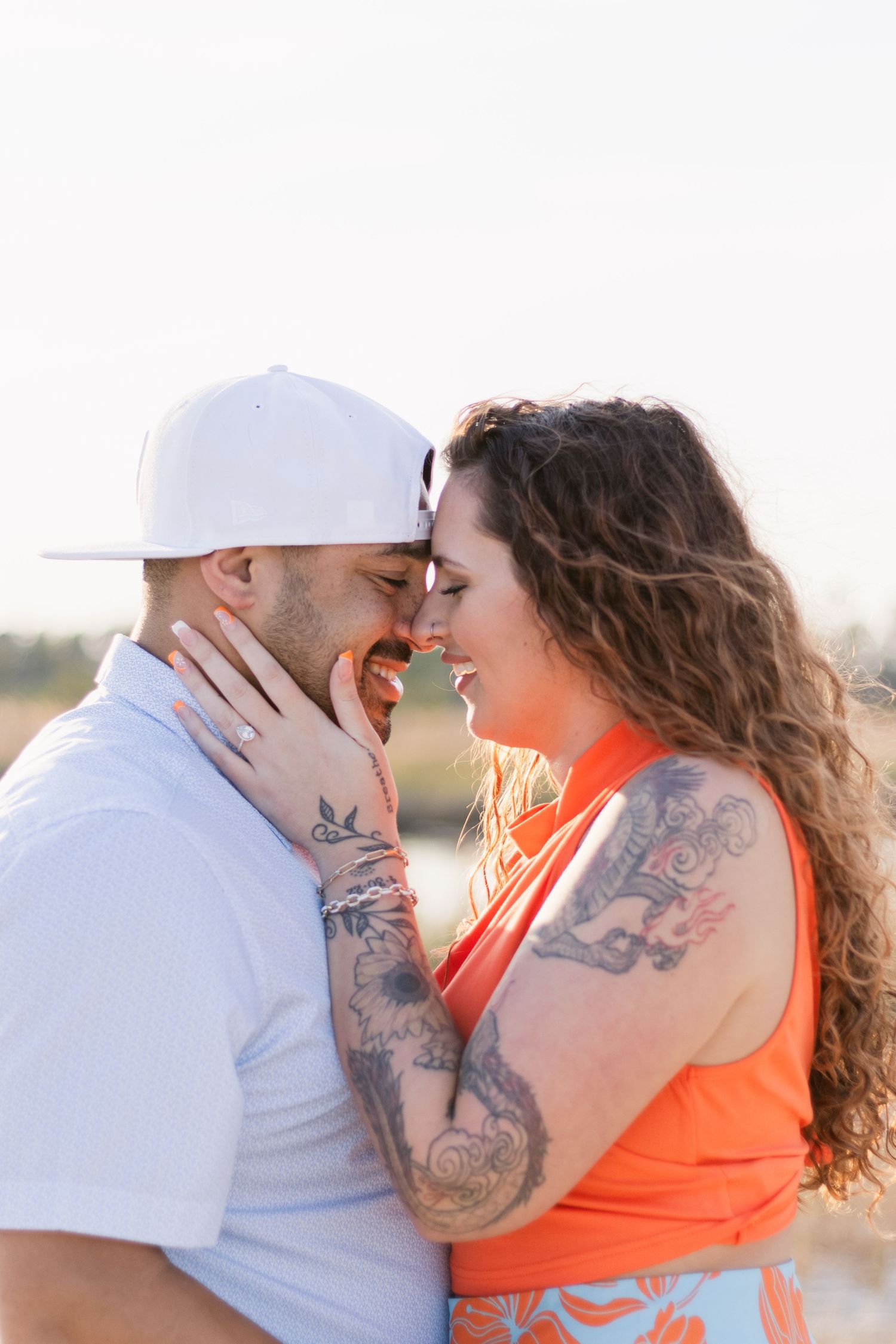 Two people in white and orange outfits share intimate moments on a beach at sunset.