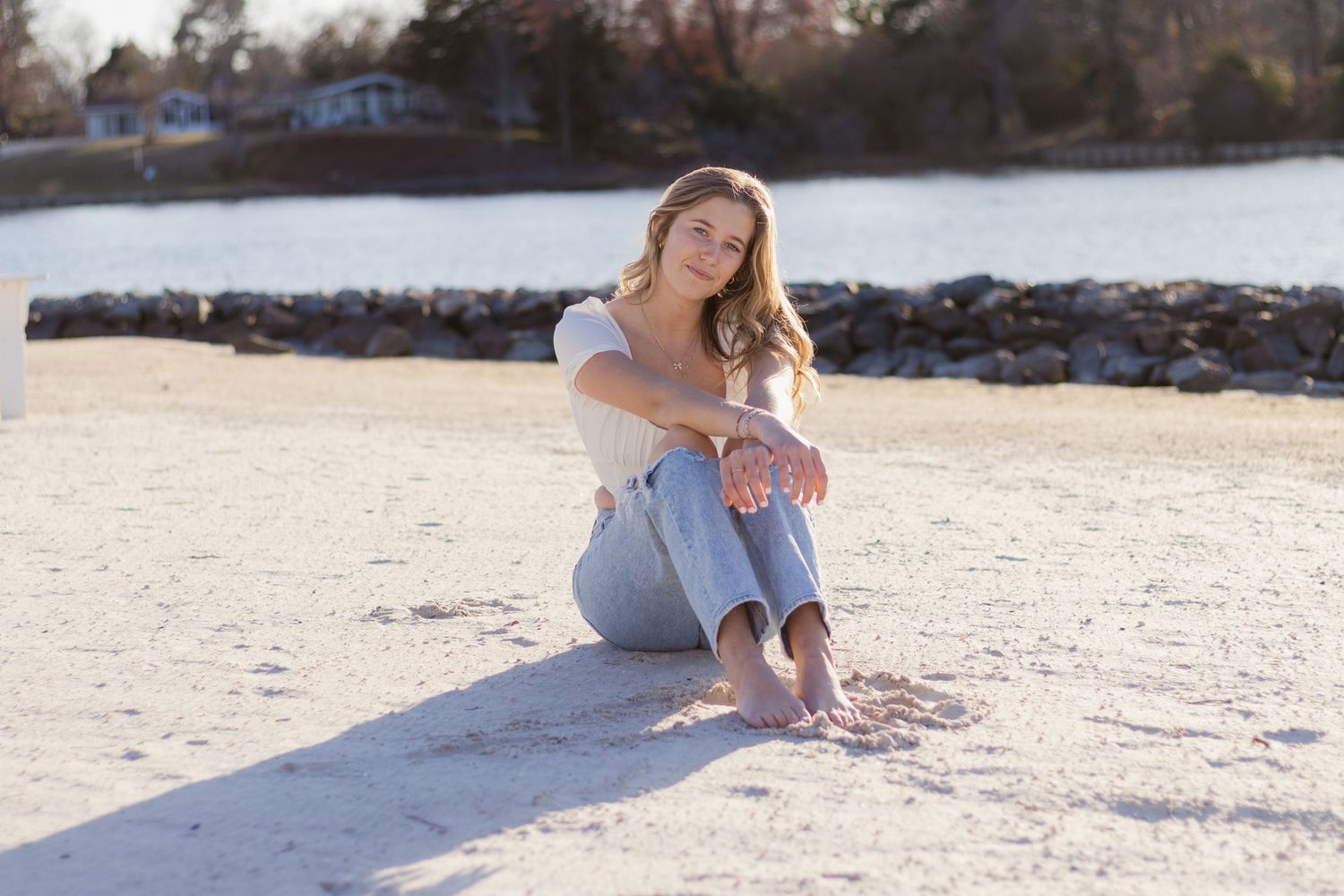 Woman in light colored dress sitting and posing on sandy tropical beach during sunset.