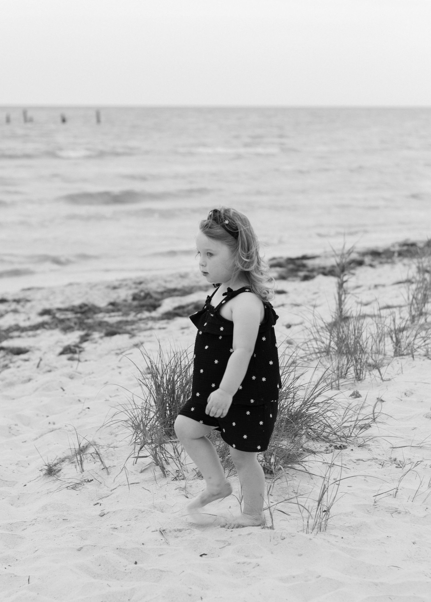 Child plays in sand dunes wearing polka dot outfit at the beach.