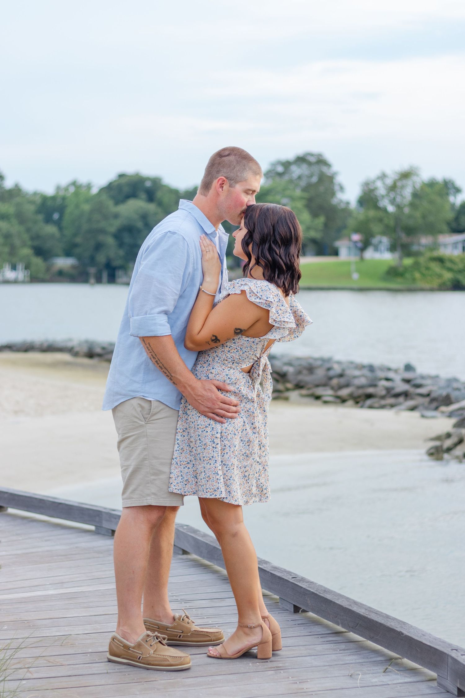 A romantic couple embraces on a wooden dock by a lake during a summer afternoon.