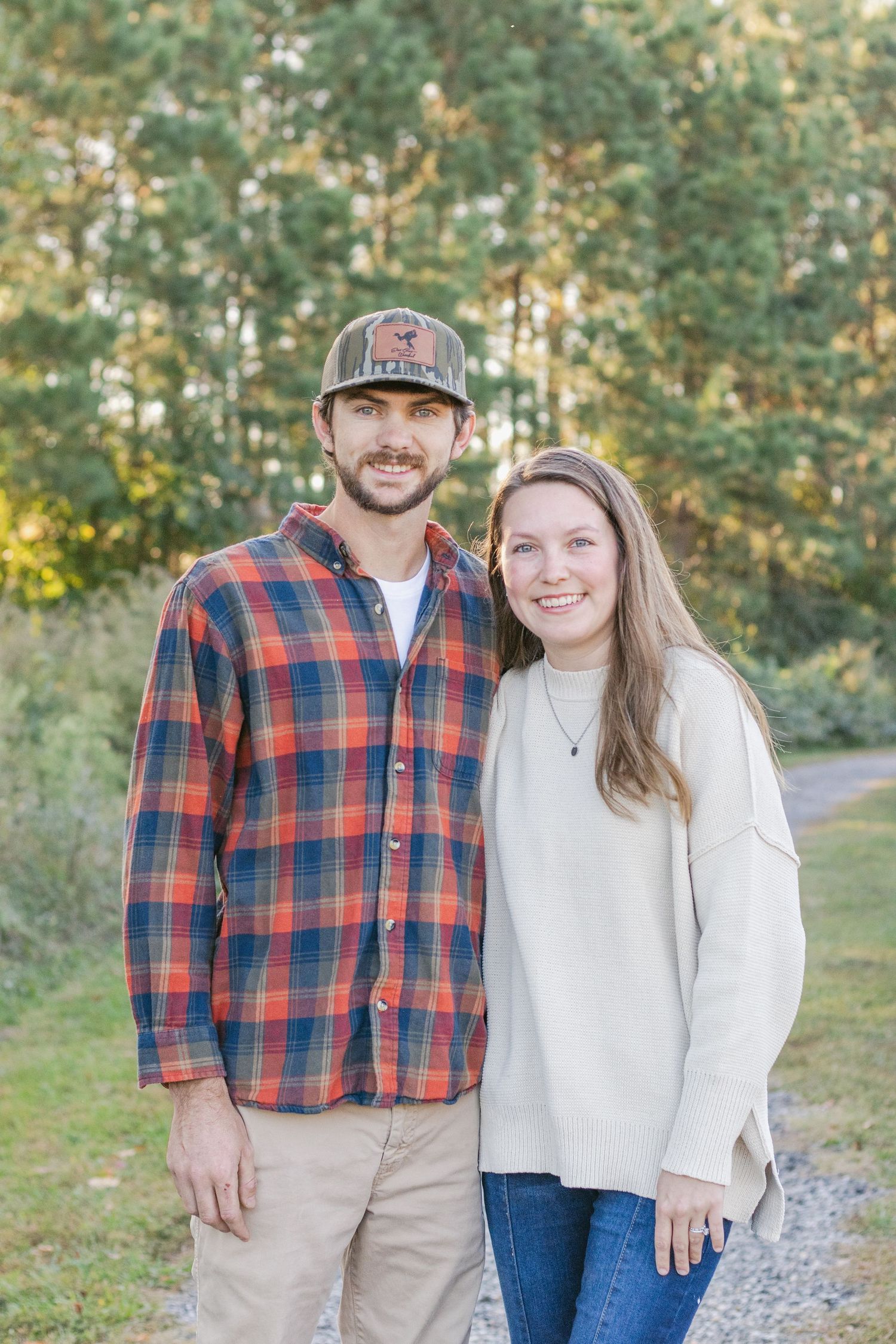 Couple in coordinating plaid and cream sweaters pose on nature trail.