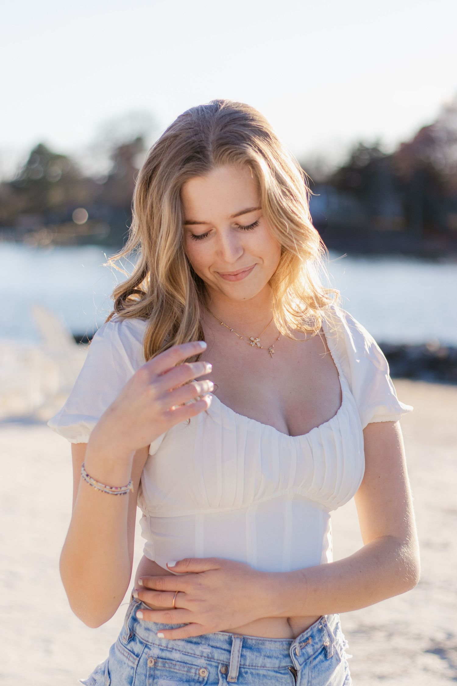 A person in a white crop top and denim shorts poses on the beach at sunset with glowing sunlit hair.
