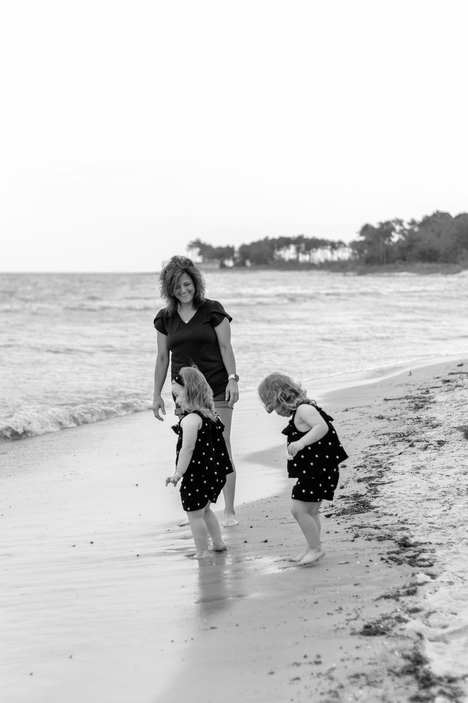Three black and white action shots capture a playful moment at a serene beach with figures bending down to explore the shore.