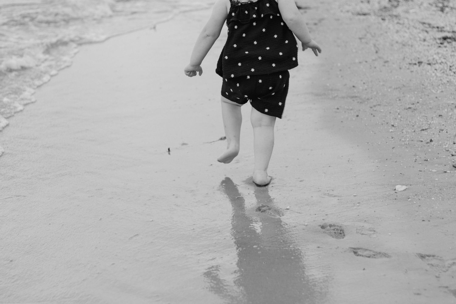 Black and white photo showing two people walking together along a sandy beach shoreline.
