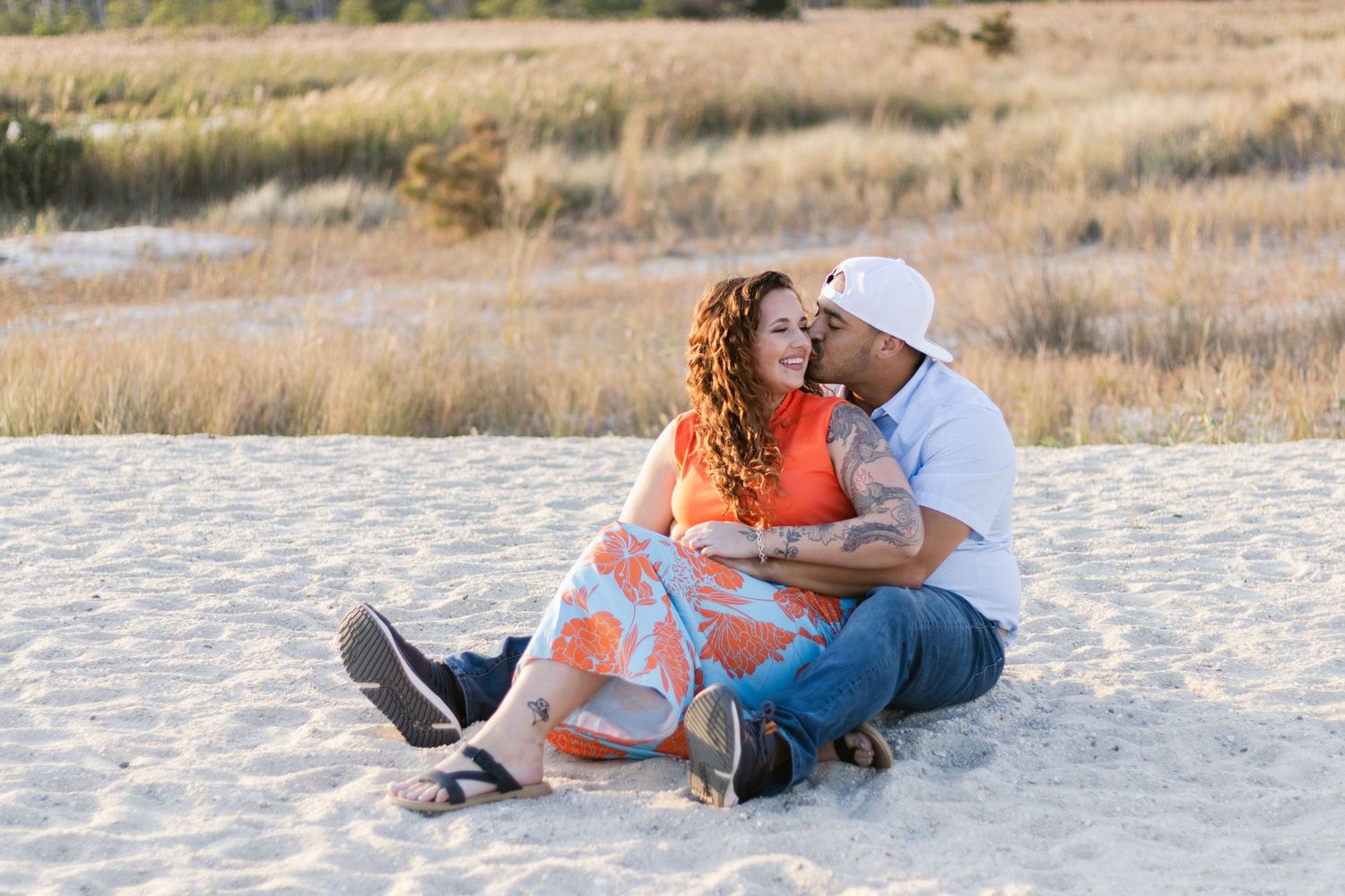 A couple in orange and denim lay together in a row of candid poses on white sand during a beach photoshoot.