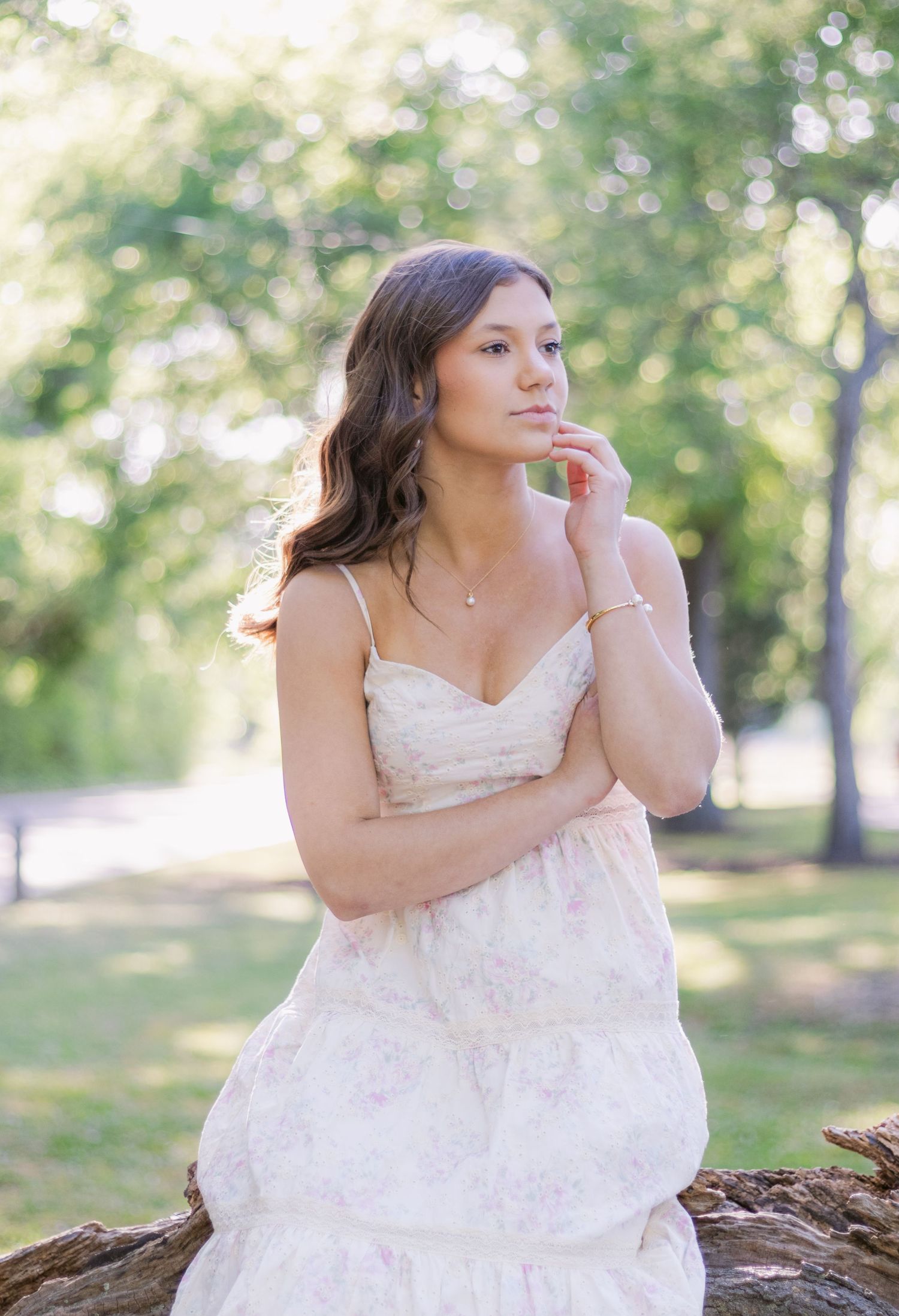 A person in a white lace wedding dress sits thoughtfully outdoors in a sunlit park setting.