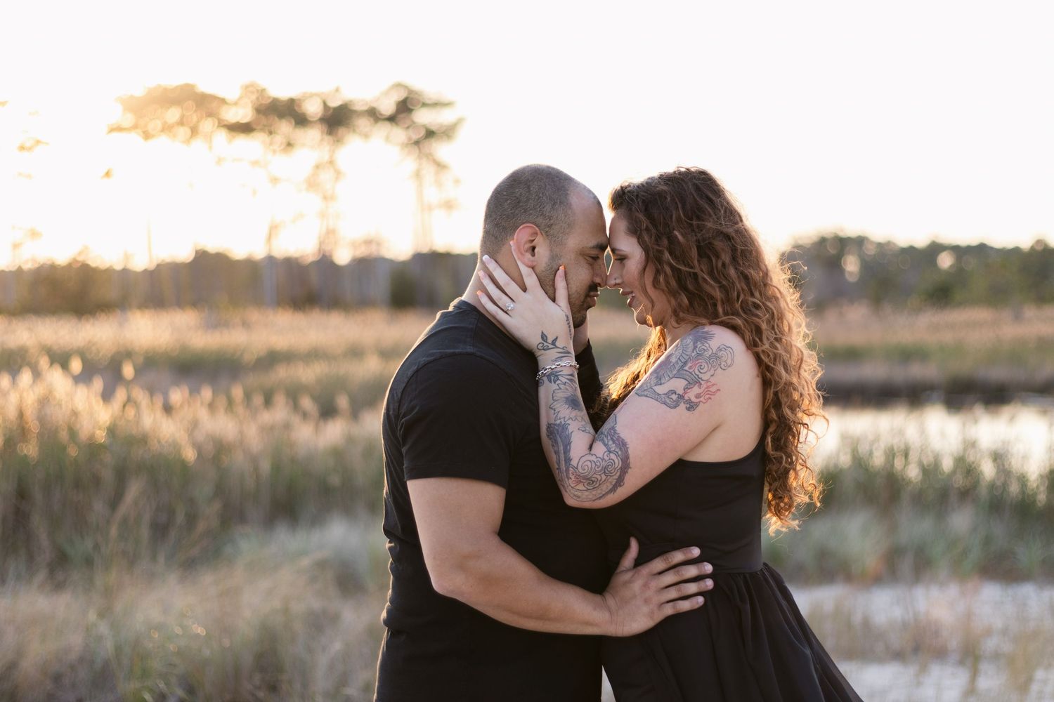 A romantic couple embraces in a golden sunset by a marsh, sharing an intimate moment against the warm evening light.