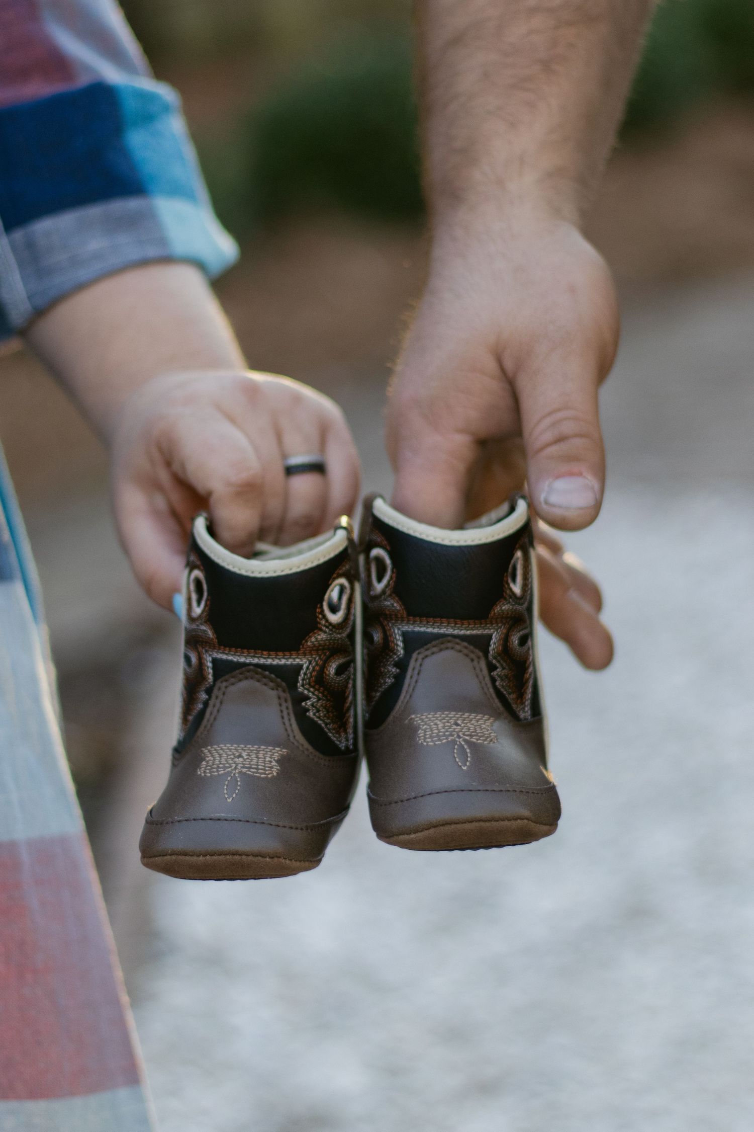 Series of hands holding and displaying different angles of small brown leather baby shoes with decorative stitching details.