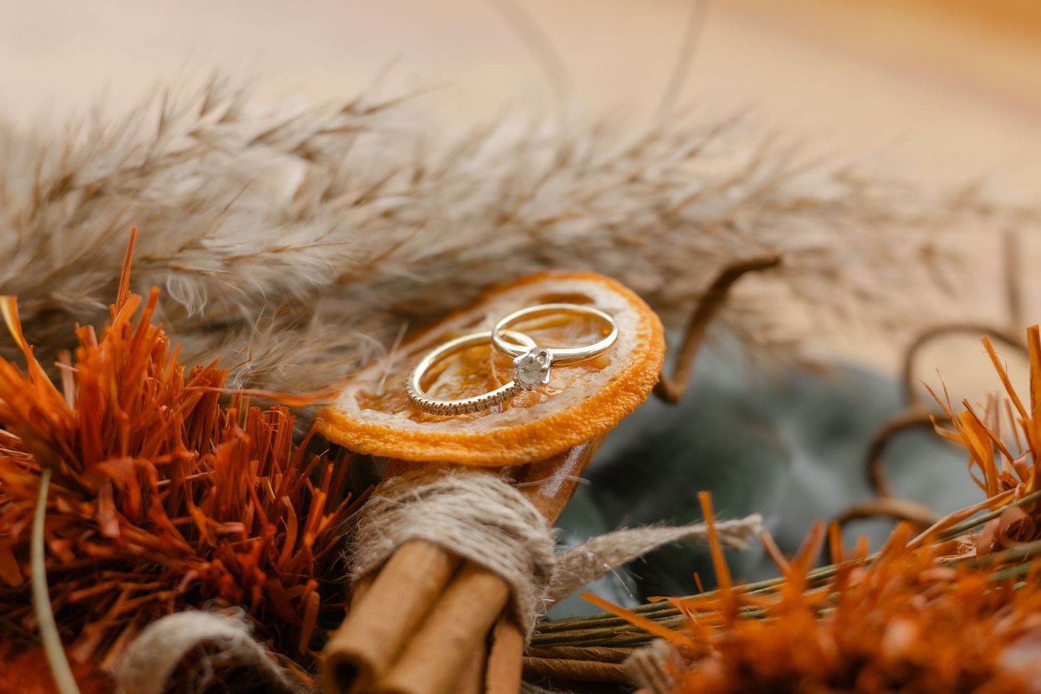 Two gold wedding rings rest on a rustic wooden surface with orange autumn leaves and feathers.