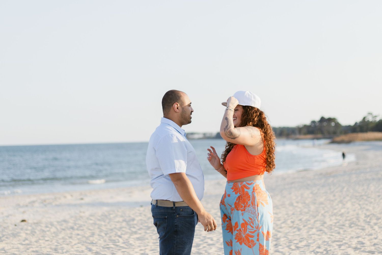 A couple at sunset on the beach wearing coordinated white and coral outfits share romantic moments.