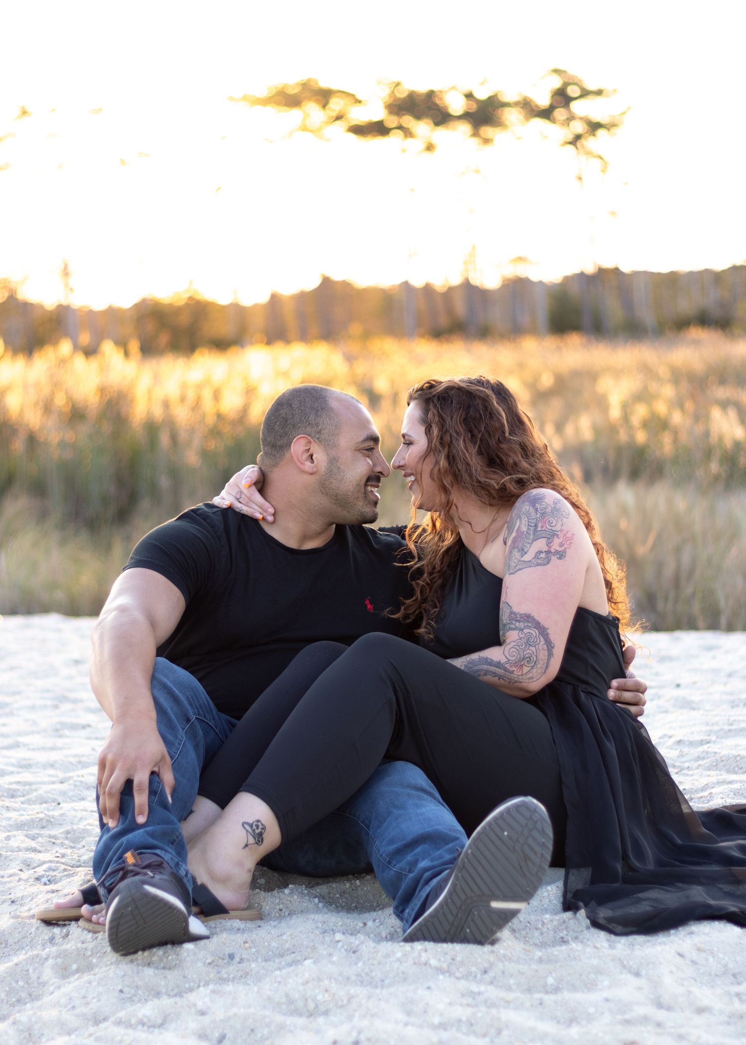 Romantic couple sitting on white sand at sunset with soft golden light illuminating the beach scene.