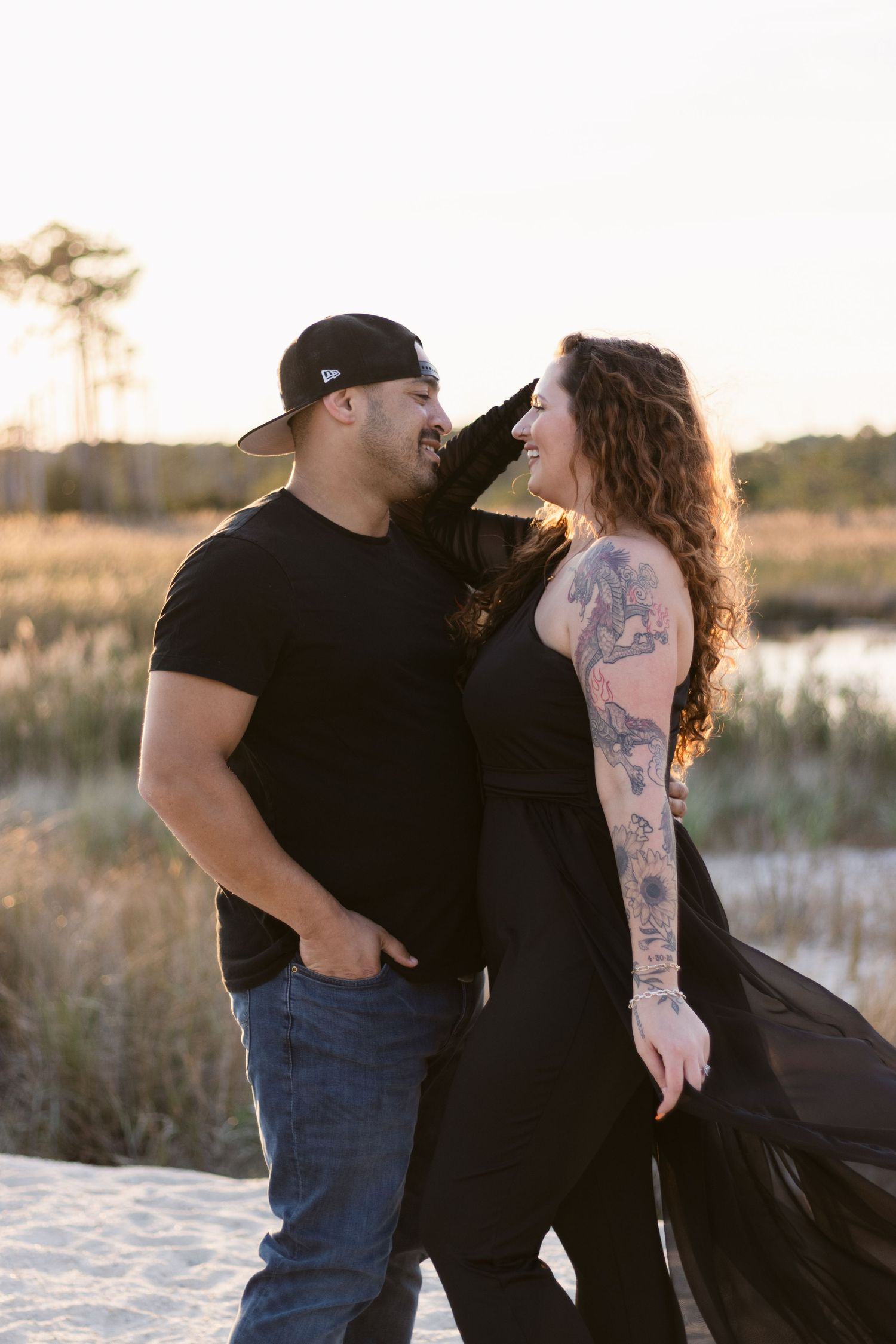 A couple shares a joyful moment together on a sandy beach at sunset in matching black outfits.