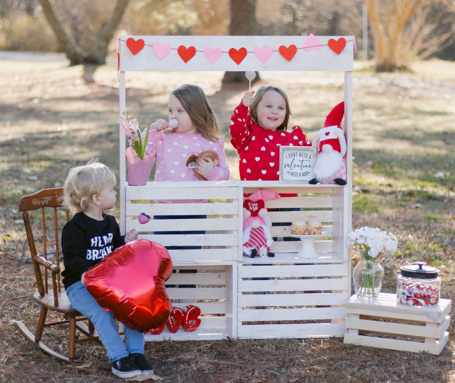 Valentine's Day themed wooden lemonade stand display with hearts decorations and festive accessories in an outdoor setting.