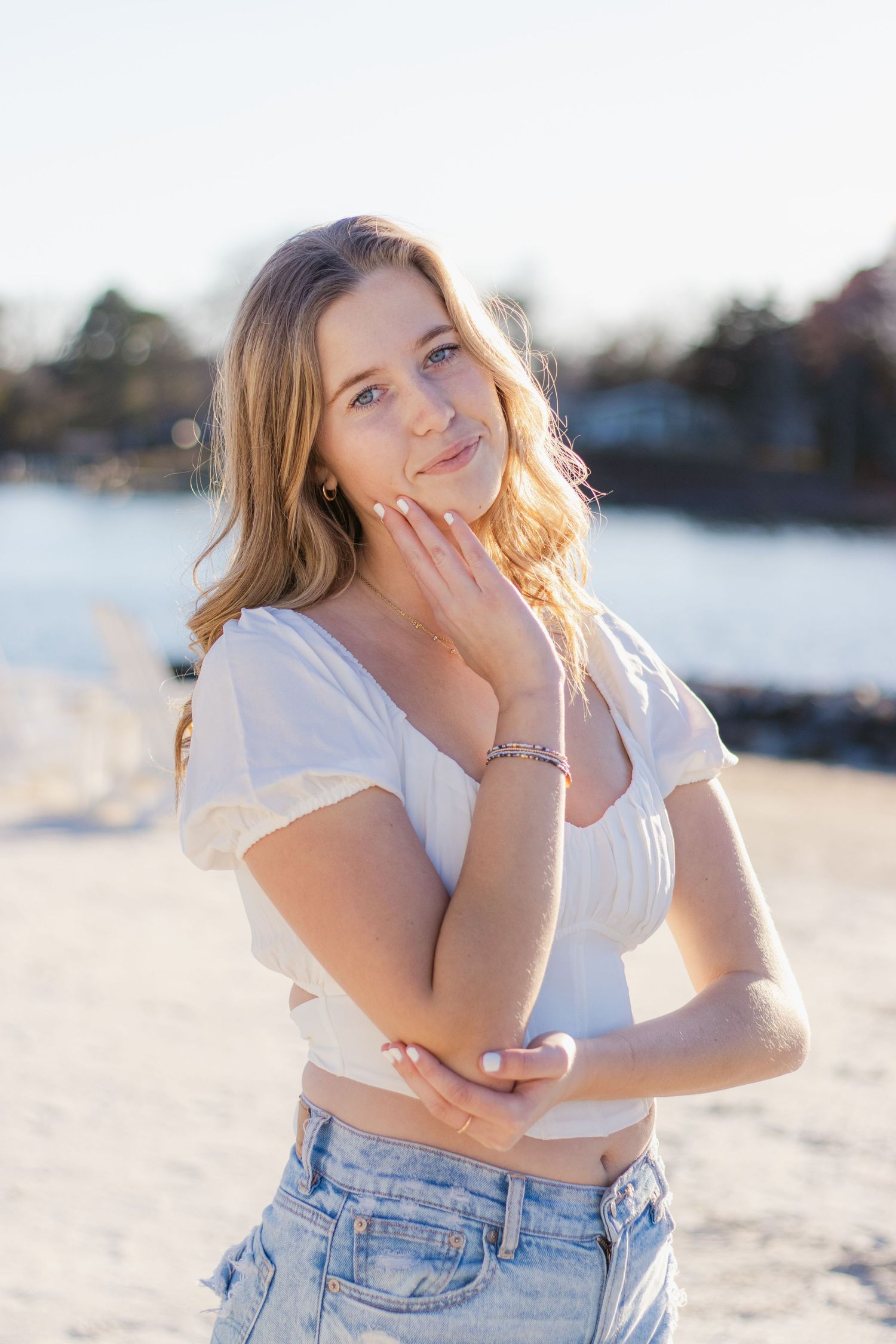 Young woman in white top and denim relaxes outdoors at beach during golden hour sunset light.