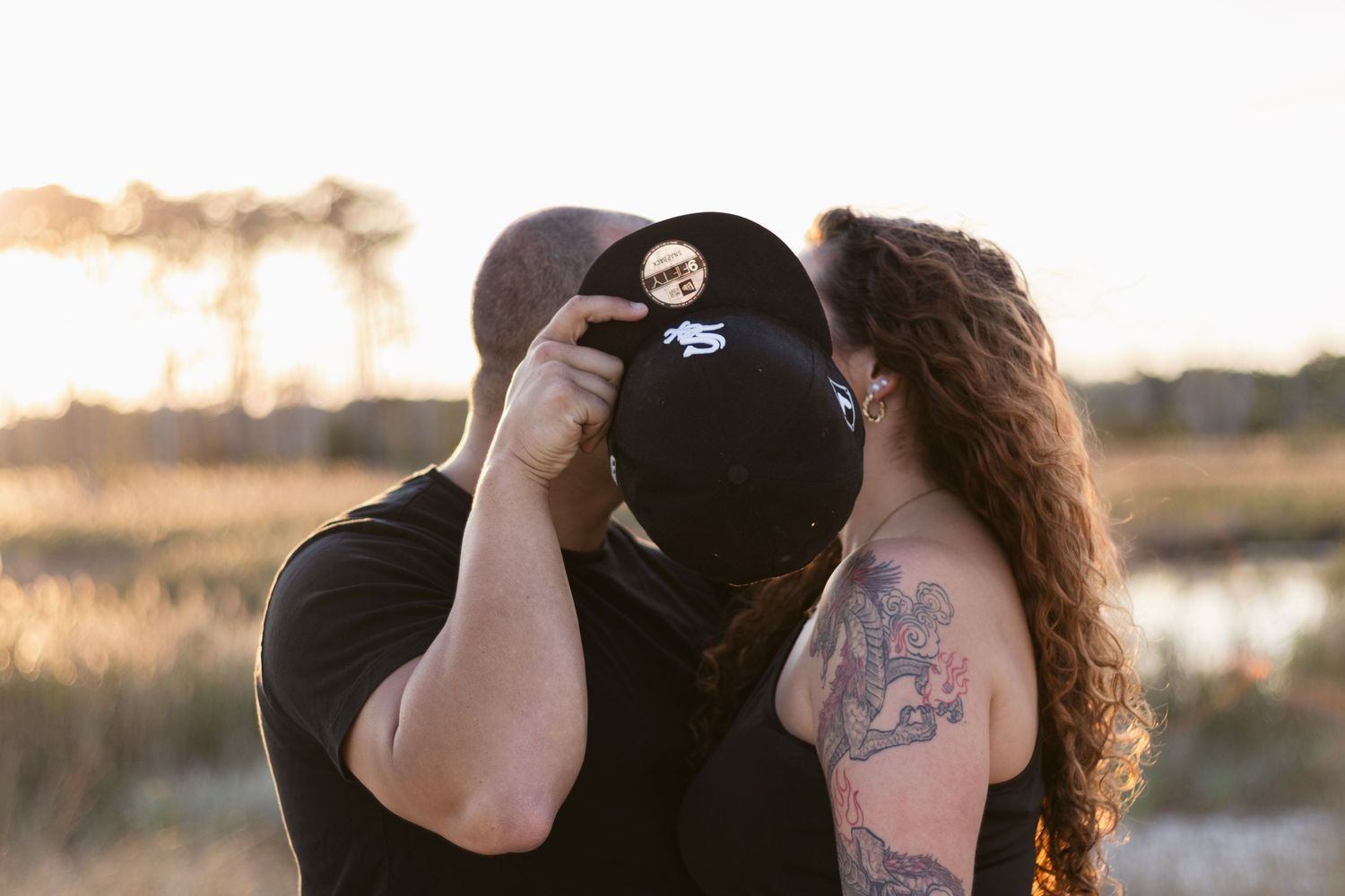 A person takes a photograph with a camera during golden hour with a tattooed individual beside them.