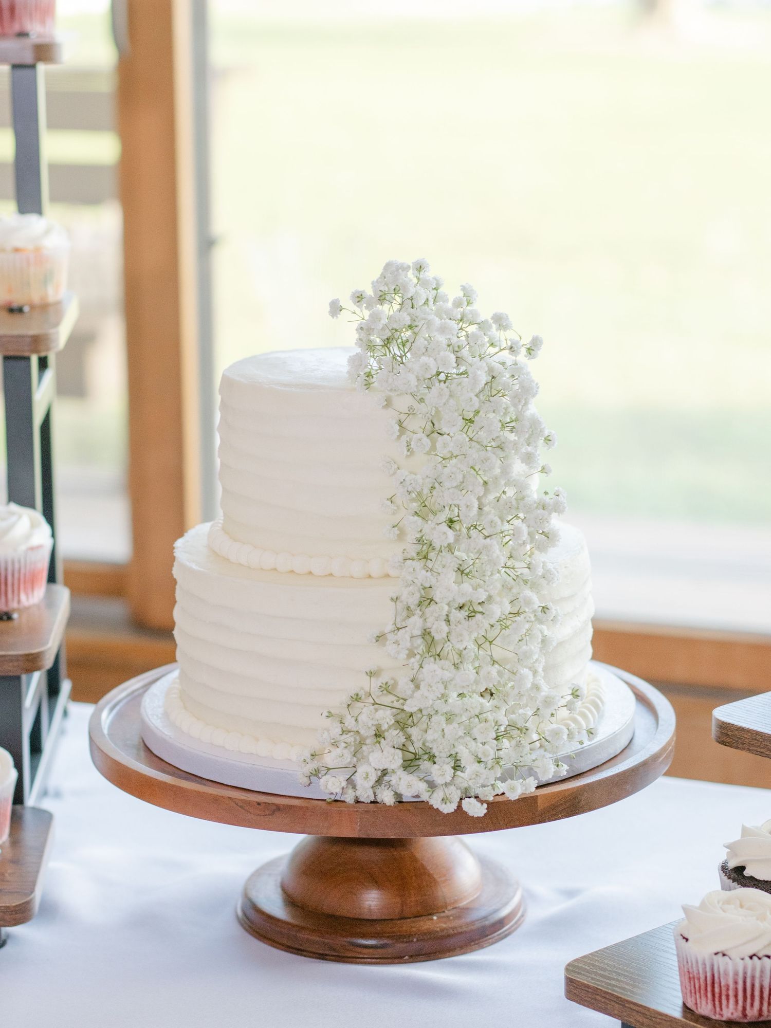 White wedding cake with textured frosting and delicate baby's breath flowers on wooden cake stand against light background.
