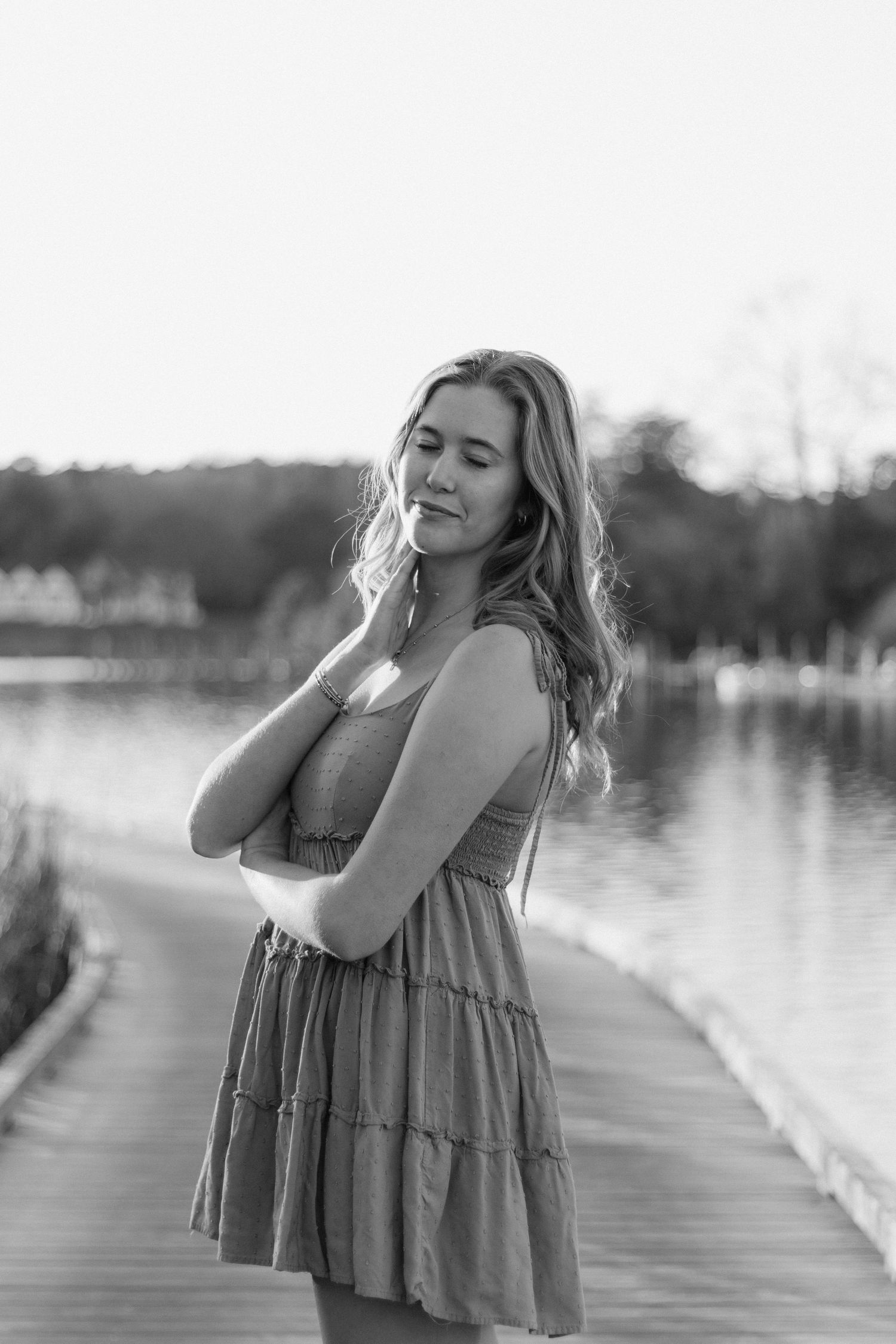 Girl in gray dress poses emotively in a series of black and white portraits on a lakeside dock at sunset.