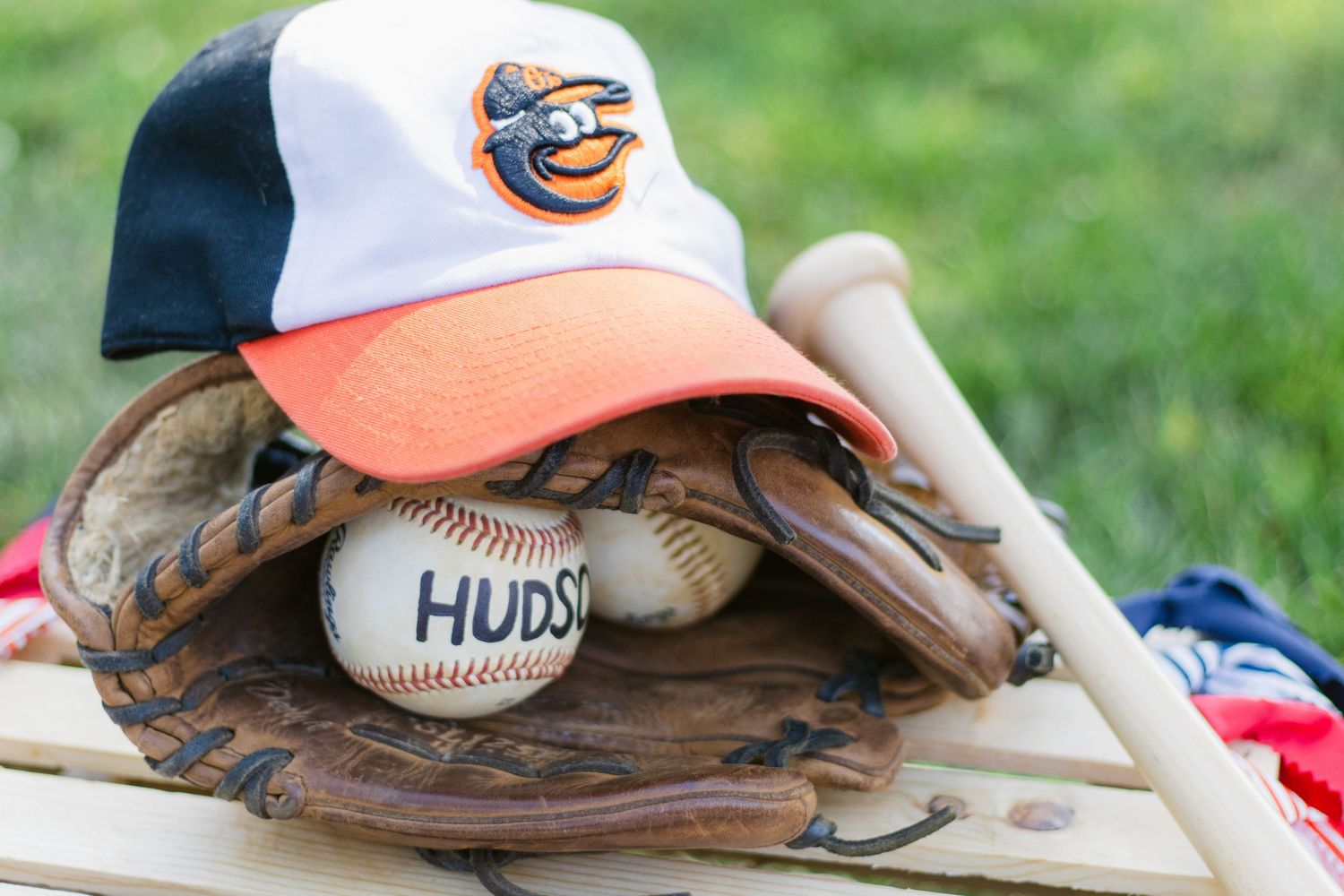 A baseball rests on a leather baseball glove with grass in the background, beside a white and orange baseball cap.