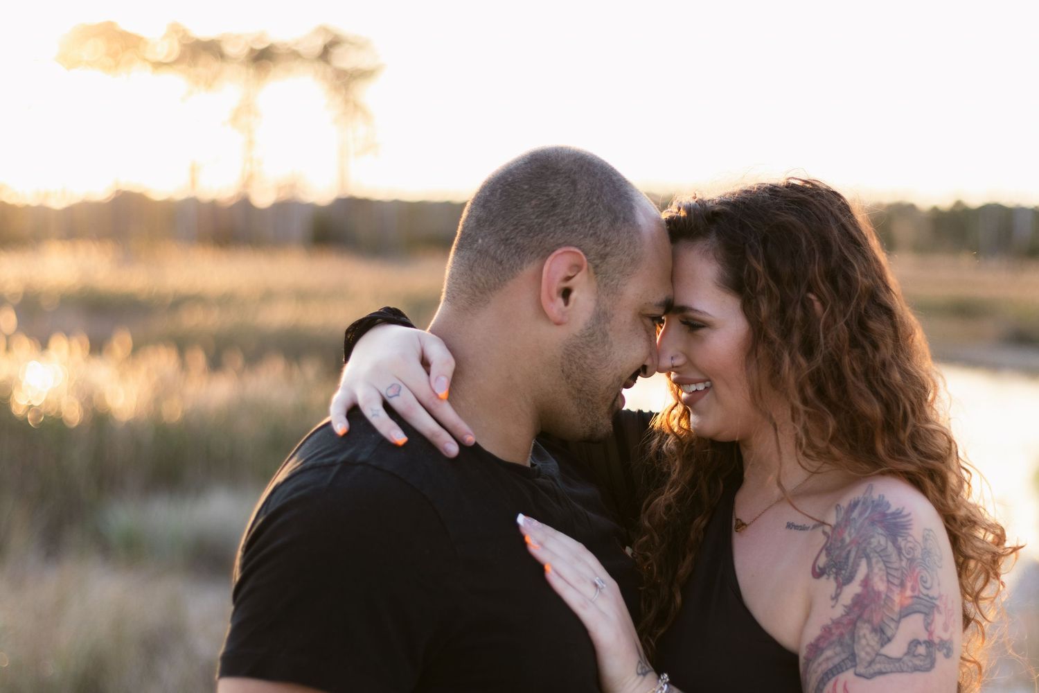 A romantic couple embraces in a golden field during sunset, with warm lighting and natural surroundings.