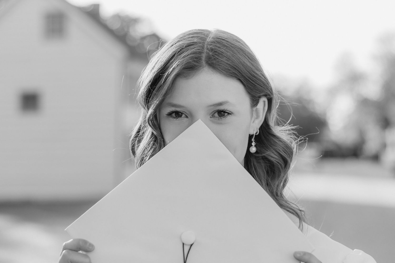 A person holds up a white piece of paper to cover the lower half of their face in a black and white photograph.