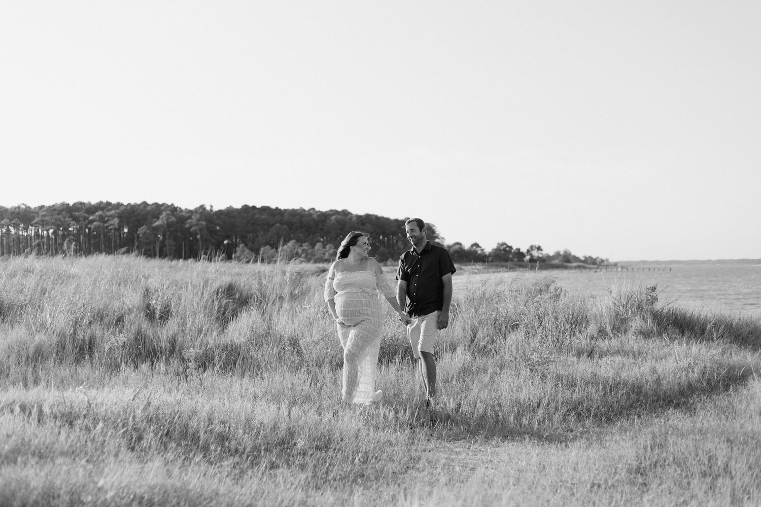 Black and white photo of a couple holding hands in a grassy field with trees in the background.