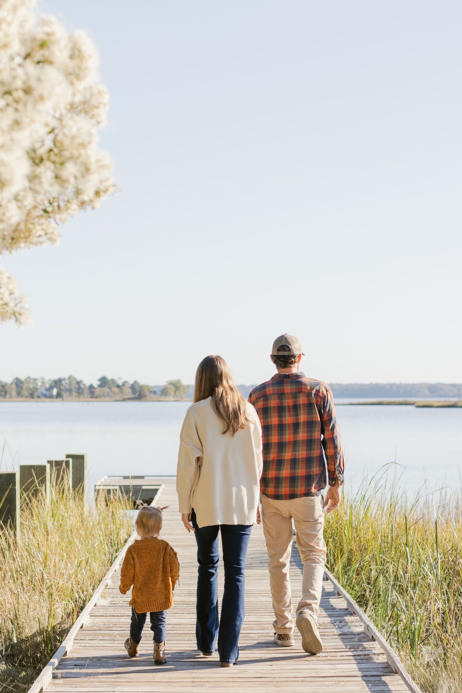 Family walks together on wooden boardwalk overlooking coastal waters.