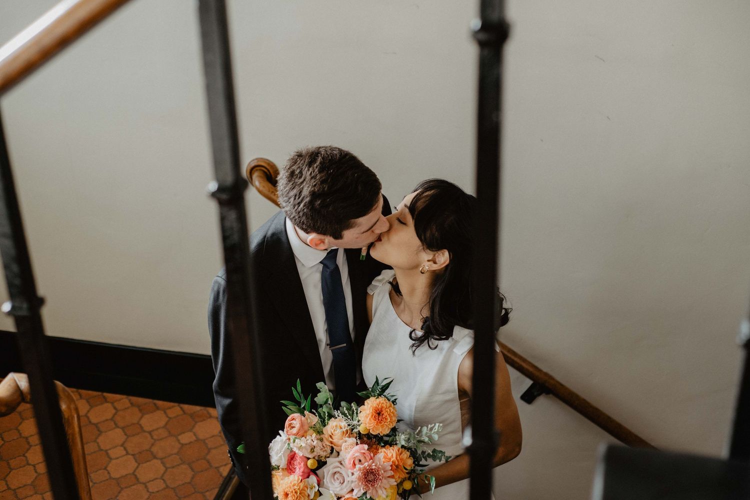 Romantic moment captured on a staircase with a beautiful bouquet of pink and peach flowers.