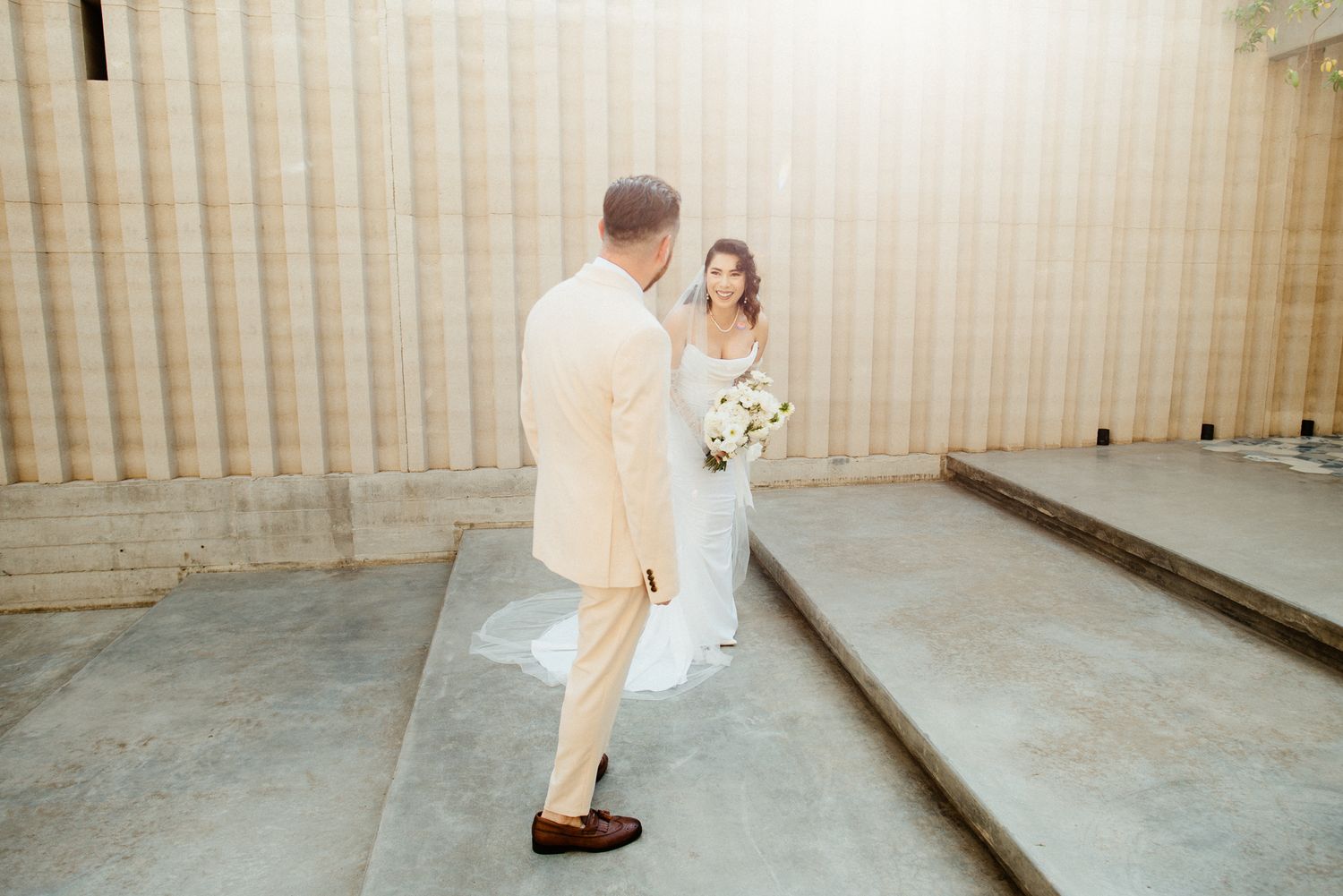 A couple shares their first look moment against a textured wall during their wedding day.