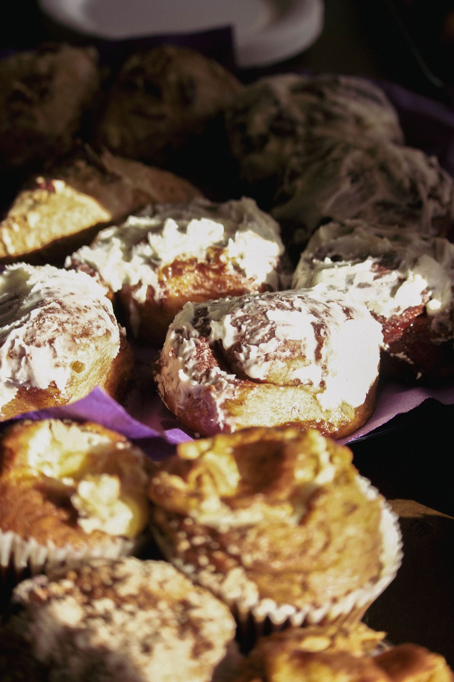 Assorted muffins and cream-topped pastries displayed on a purple paper plate at a bakery event.