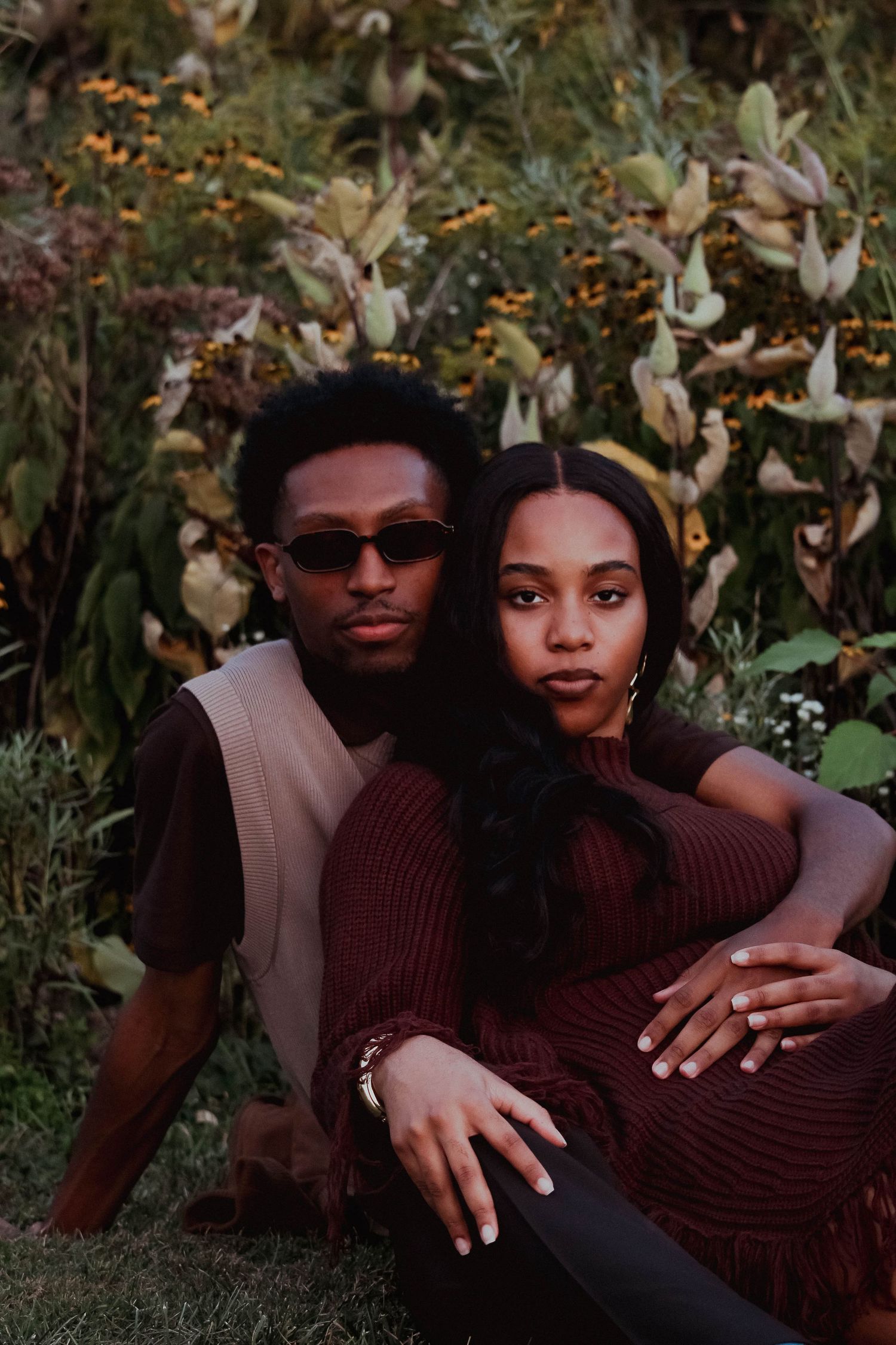 Couple sitting together in a garden, wearing coordinated brown earth-tone outfits among flowers.